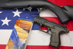 A concept image of liberty showing a pistol and rifle with the constitution booklet on the American flag,